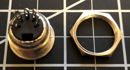 The back of a MIDI connector next to a machine nut