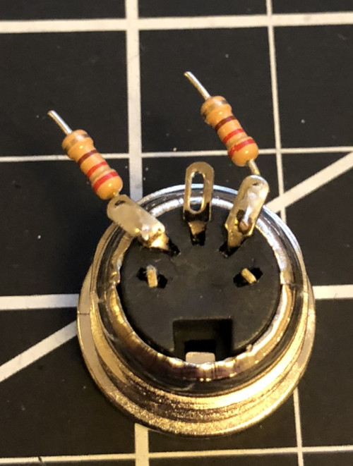 The back of a MIDI connector with the two outer pins clipped and the three inner pins bent up.  Resistors are soldered to the left-most pin and the right-most pin.  The other leads of the resistors are short.