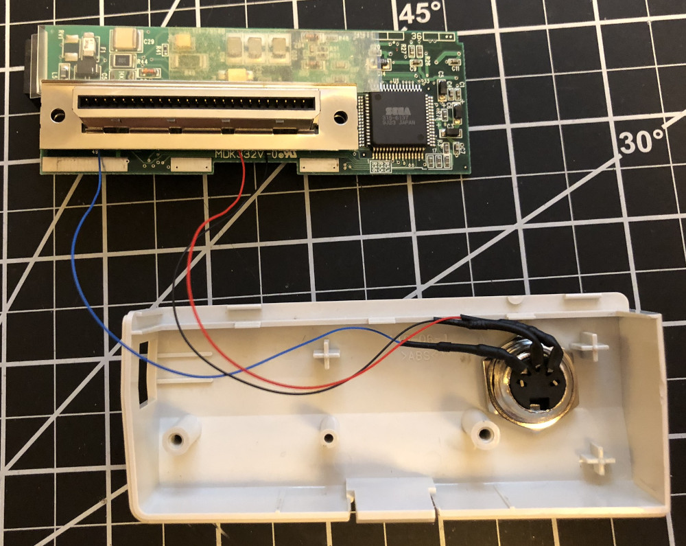 A Dreamcast modem PCB.  The G2 connector has a black wire soldered to pin 11 (ground), a red wire soldered to pin 17 (+5V), and a blue wire soldered to pin 49 (MIDI OUT).  The wires are soldered to the back of a MIDI connector that is sticking through the modem's plastic case.