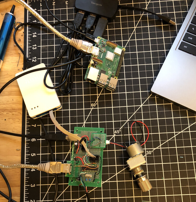 A photo of the the test setup with the custom hardware connected to a motorized potentiometer and a Raspberry Pi via HDMI